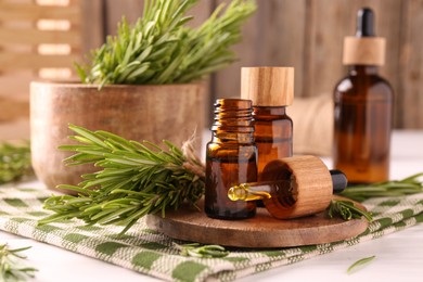 Photo of Essential oil in bottles, dropper and rosemary on white wooden table