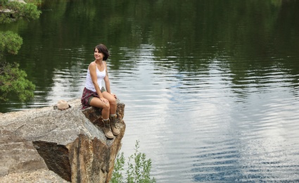 Young woman on rocky mountain near lake. Camping season