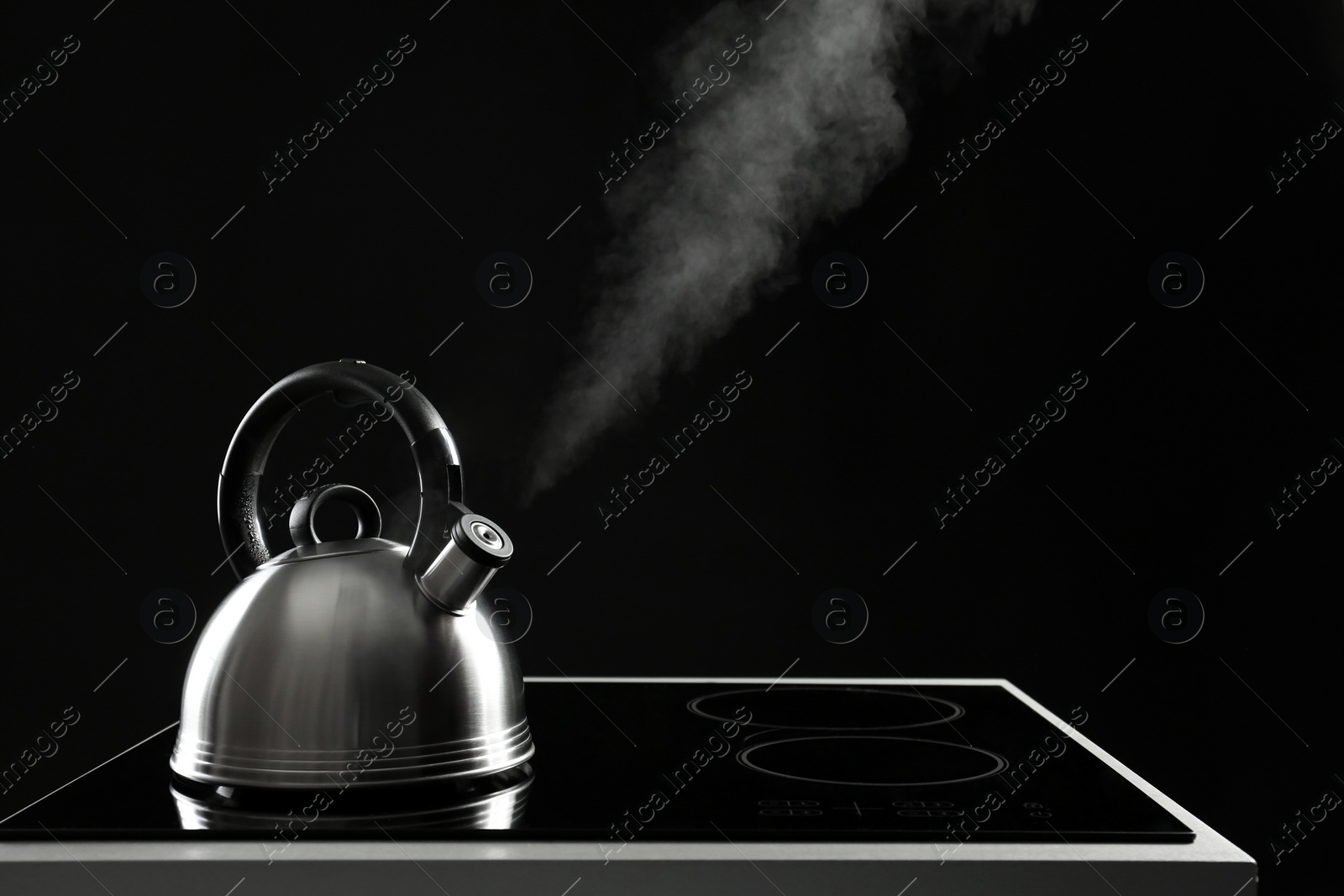 Photo of Modern kettle with whistle on stove against black background, space for text