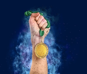 Image of Winner raising hand with gold medal surrounded by fume and shatters on blue background, closeup