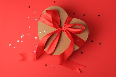 Photo of Beautiful heart shaped gift box with bow and confetti on red background, top view