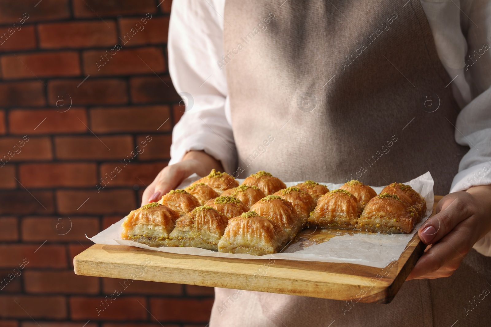 Photo of Woman with delicious sweet baklava against brick wall, closeup