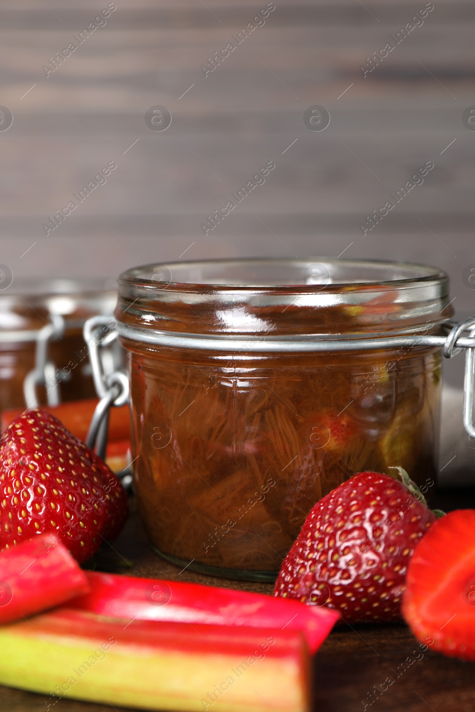 Photo of Jar of tasty rhubarb jam, fresh stems and strawberries on wooden table. Space for text