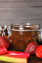 Jar of tasty rhubarb jam, fresh stems and strawberries on wooden table. Space for text