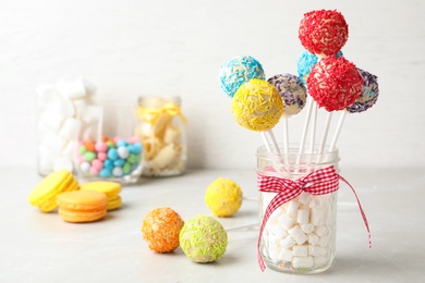 Photo of Yummy bright cake pops in glass jar full of marshmallows on table. Space for text