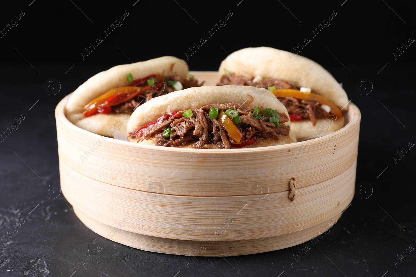 Photo of Delicious gua bao in bamboo steamer on black table