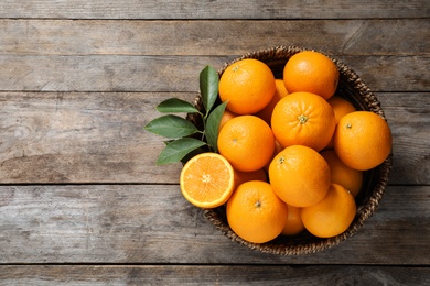 Photo of Wicker bowl with ripe oranges on wooden background, top view. Space for text