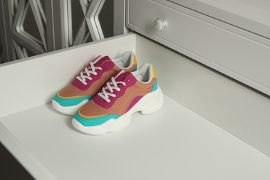 Photo of Colorful sneakers in empty drawer. Footwear storage