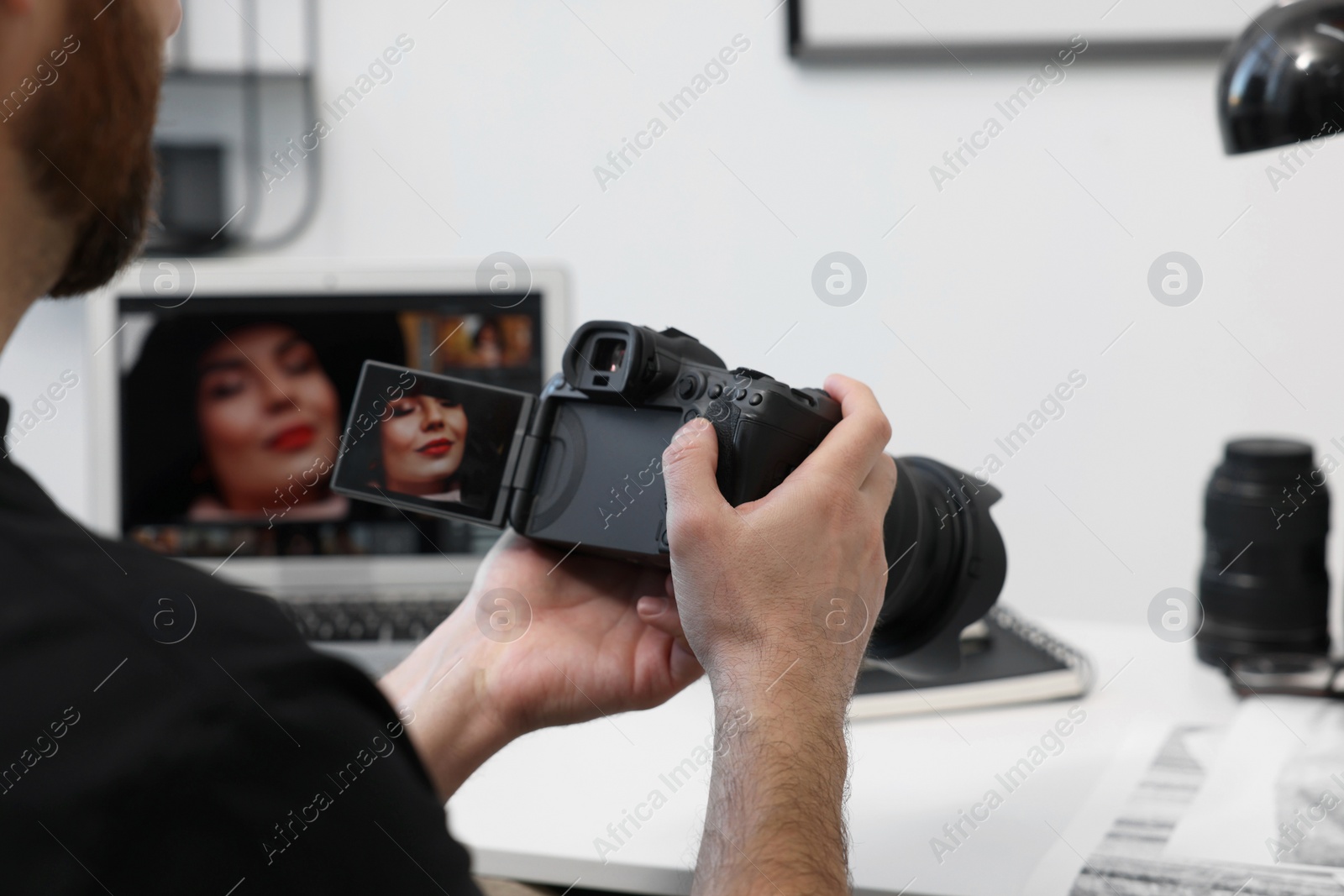 Photo of Professional photographer with digital camera at table indoors, closeup