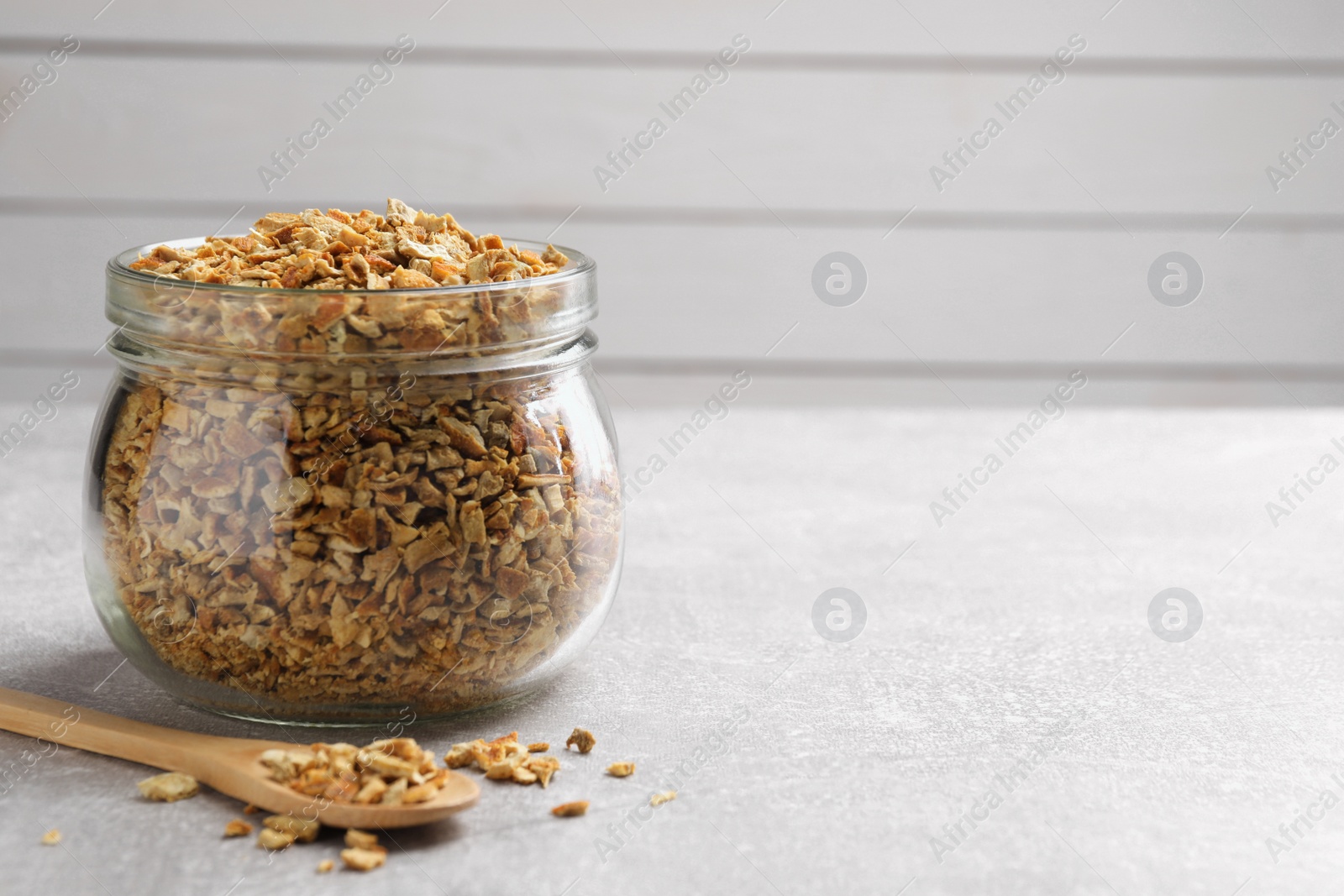 Photo of Jar and spoon with dried orange zest seasoning on light grey table. Space for text