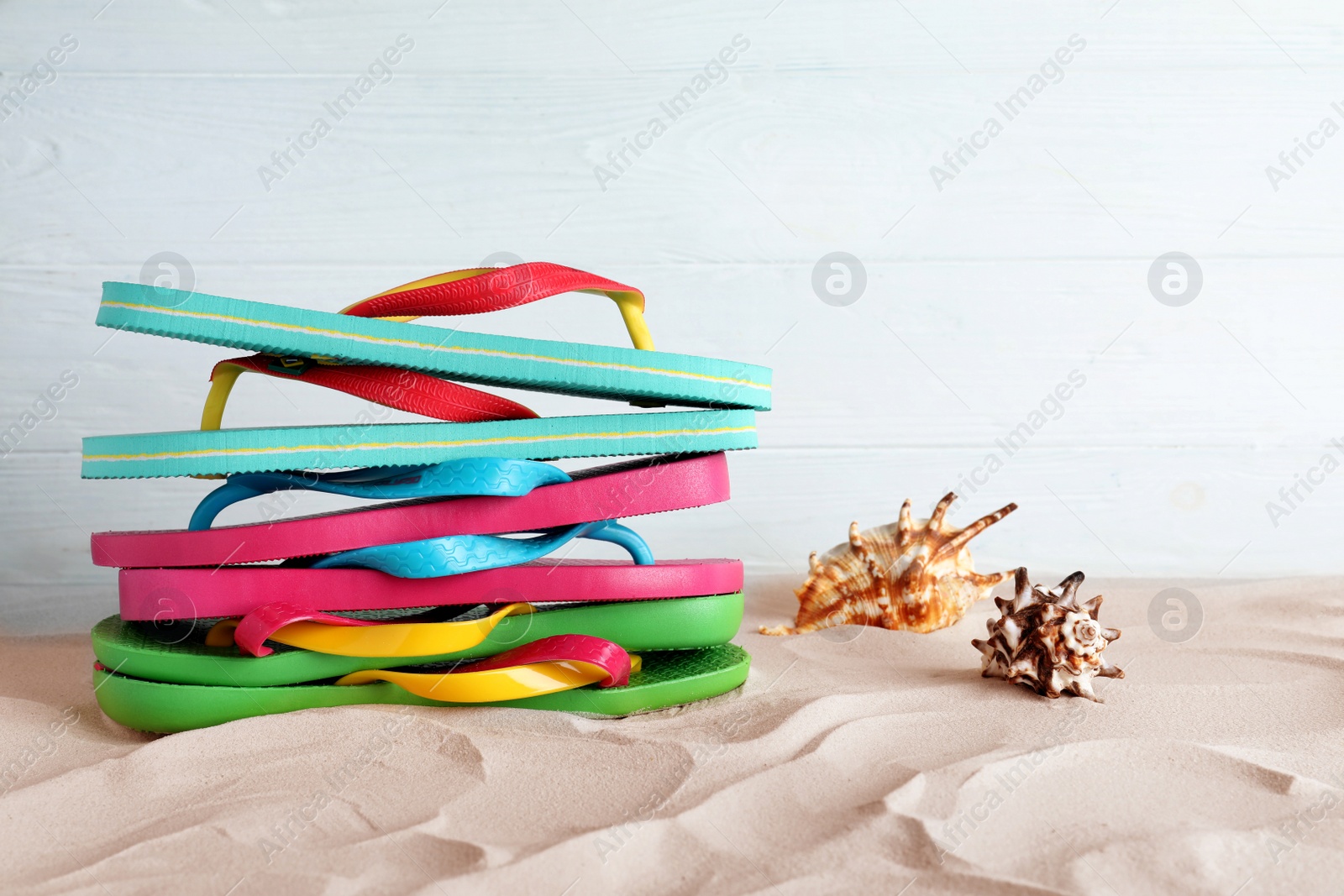 Photo of Many different flip flops and seashells on sand against white background