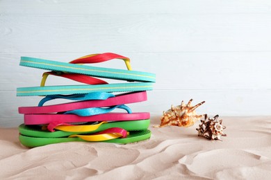 Photo of Many different flip flops and seashells on sand against white background