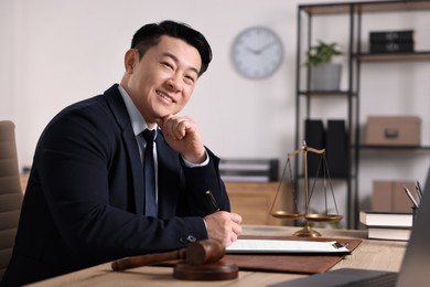 Photo of Happy notary writing notes at wooden table in office