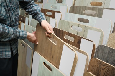 Photo of Man choosing wooden flooring among different samples in shop, closeup