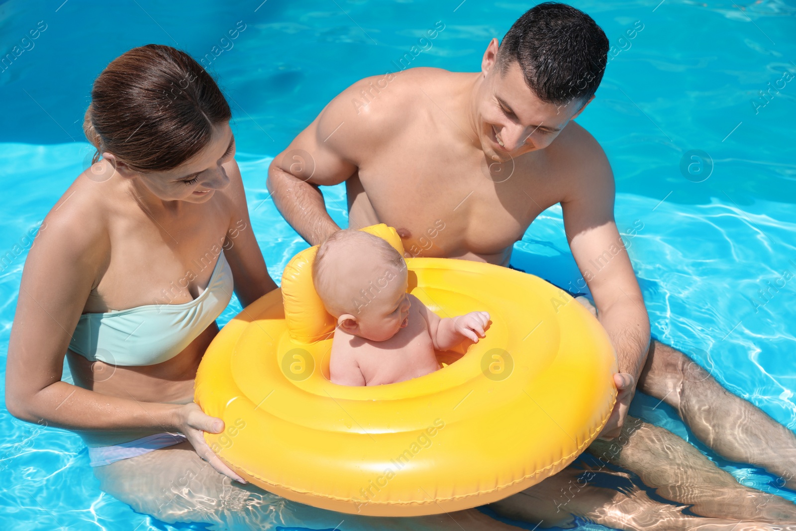 Photo of Happy parents with little baby in swimming pool on sunny day, outdoors