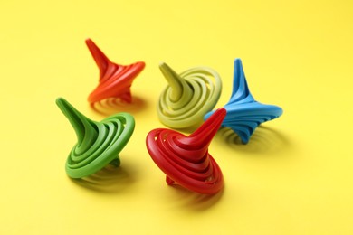 Photo of Many colorful spinning tops on yellow background, closeup