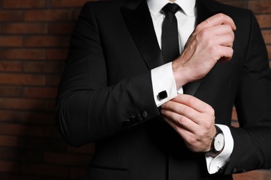 Photo of Man wearing stylish suit and cufflinks near brick wall, closeup