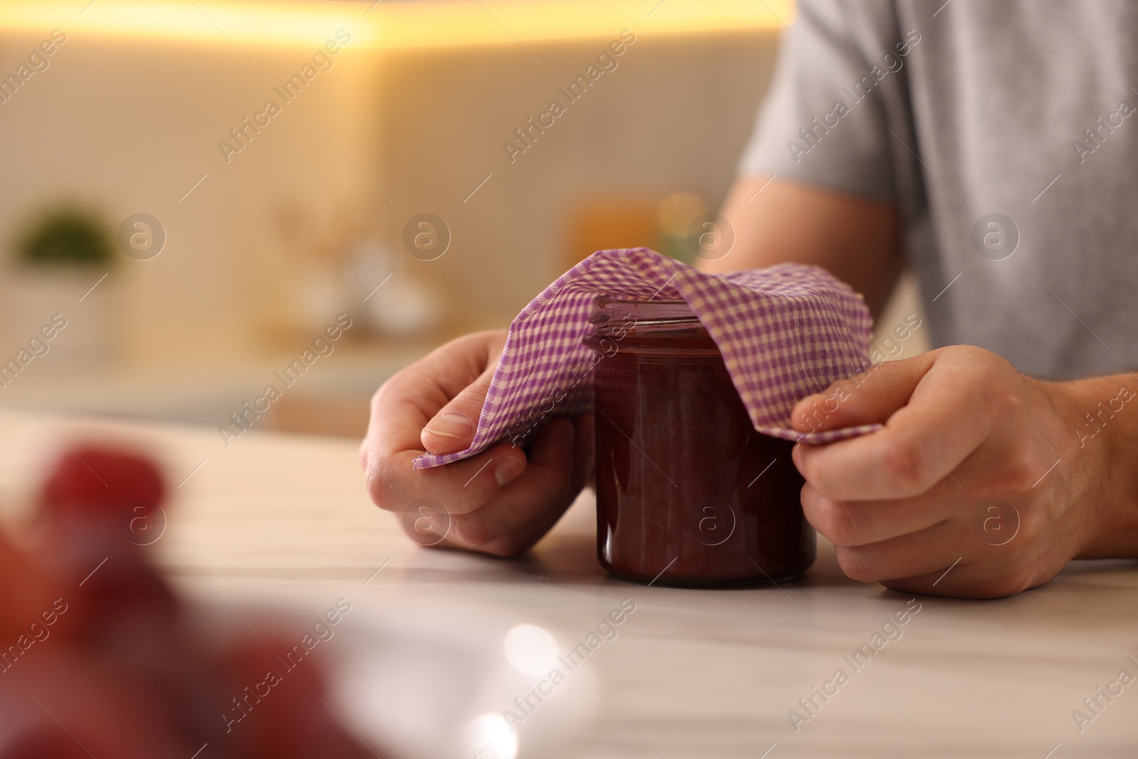 Photo of Man packing jar of jam into beeswax food wrap at light table in kitchen, closeup