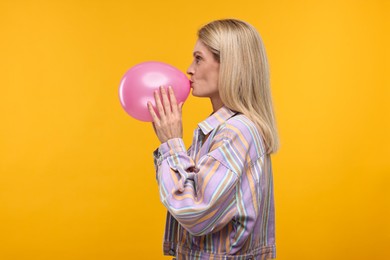 Woman blowing up balloon on yellow background
