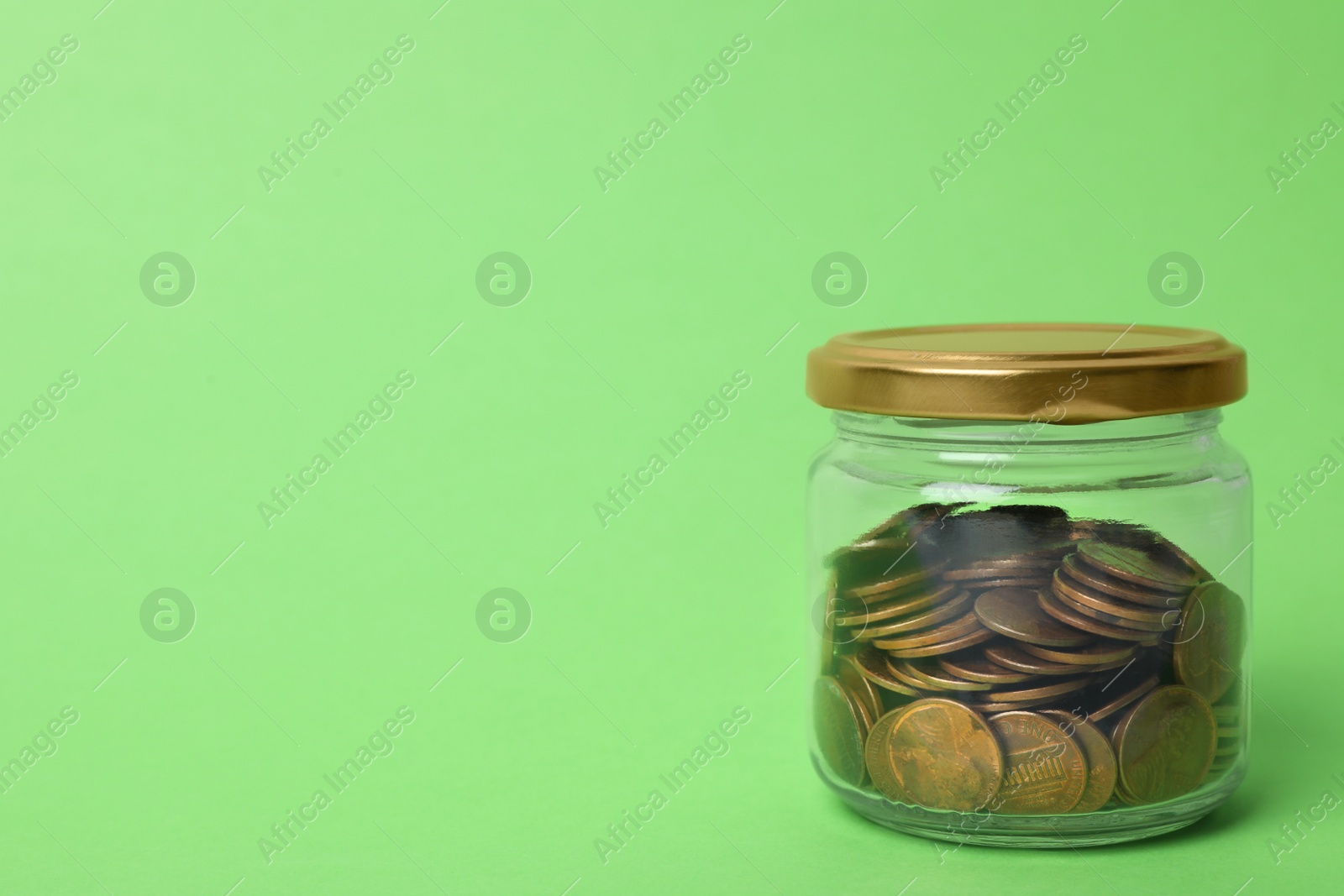 Photo of Glass jar with coins on light green background, space for text