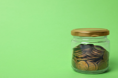 Glass jar with coins on light green background, space for text