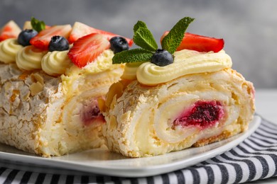 Photo of Tasty meringue roll with jam, cream, strawberry, blueberry and mint on plate, closeup