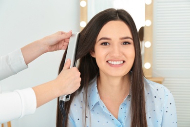 Photo of Hairdresser using modern flat iron to style client's hair in salon