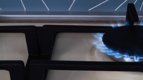 Photo of White gas cooktop with turned on burner, closeup
