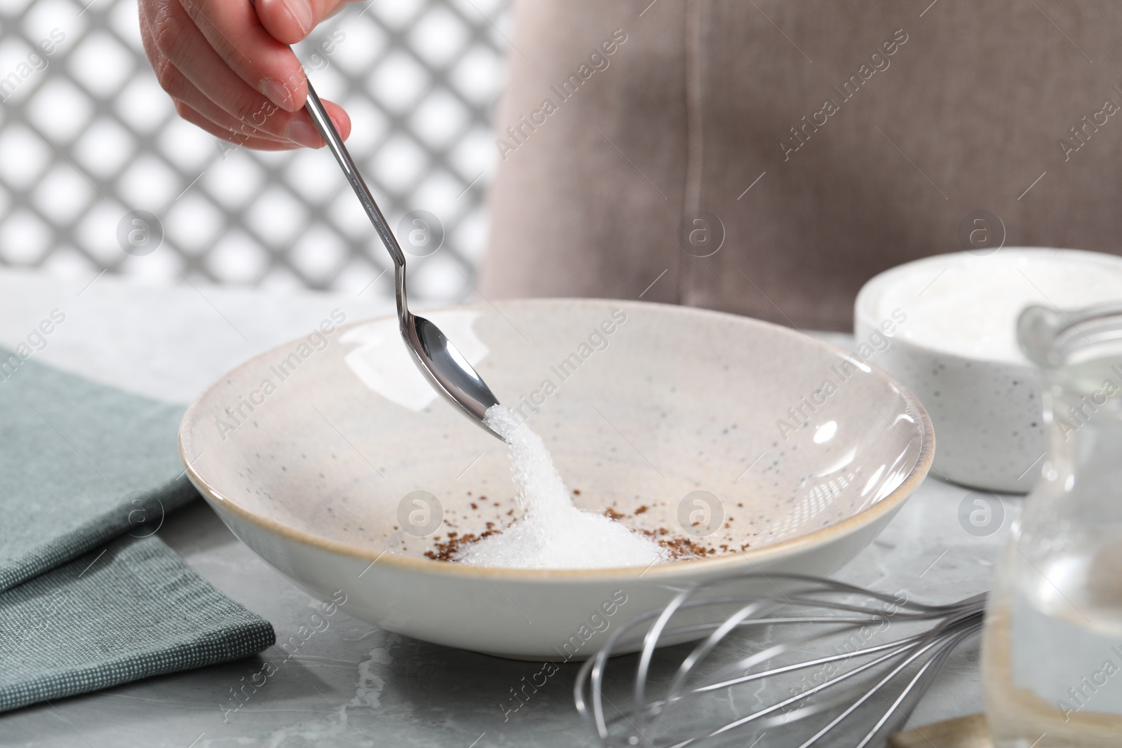 Photo of Woman pouring sugar into bowl at light gray table, closeup. Making dalgona coffee