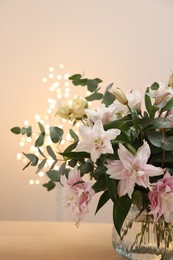 Photo of Bouquet of beautiful lily flowers in vase on table against beige background with blurred lights