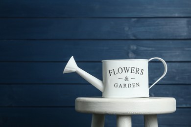 Photo of White metal watering can on table against blue wooden background, space for text