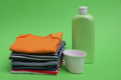 Photo of Stack of baby clothes and laundry detergents on light green background