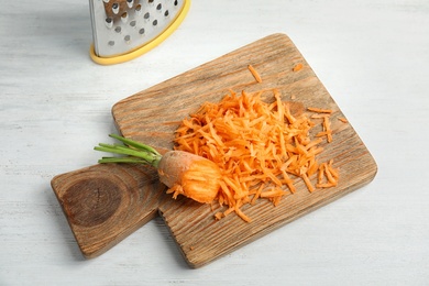 Wooden board with grated carrot on table