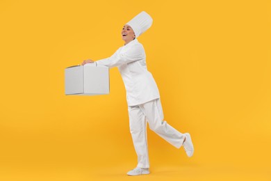 Photo of Happy professional confectioner in uniform holding cake box on yellow background