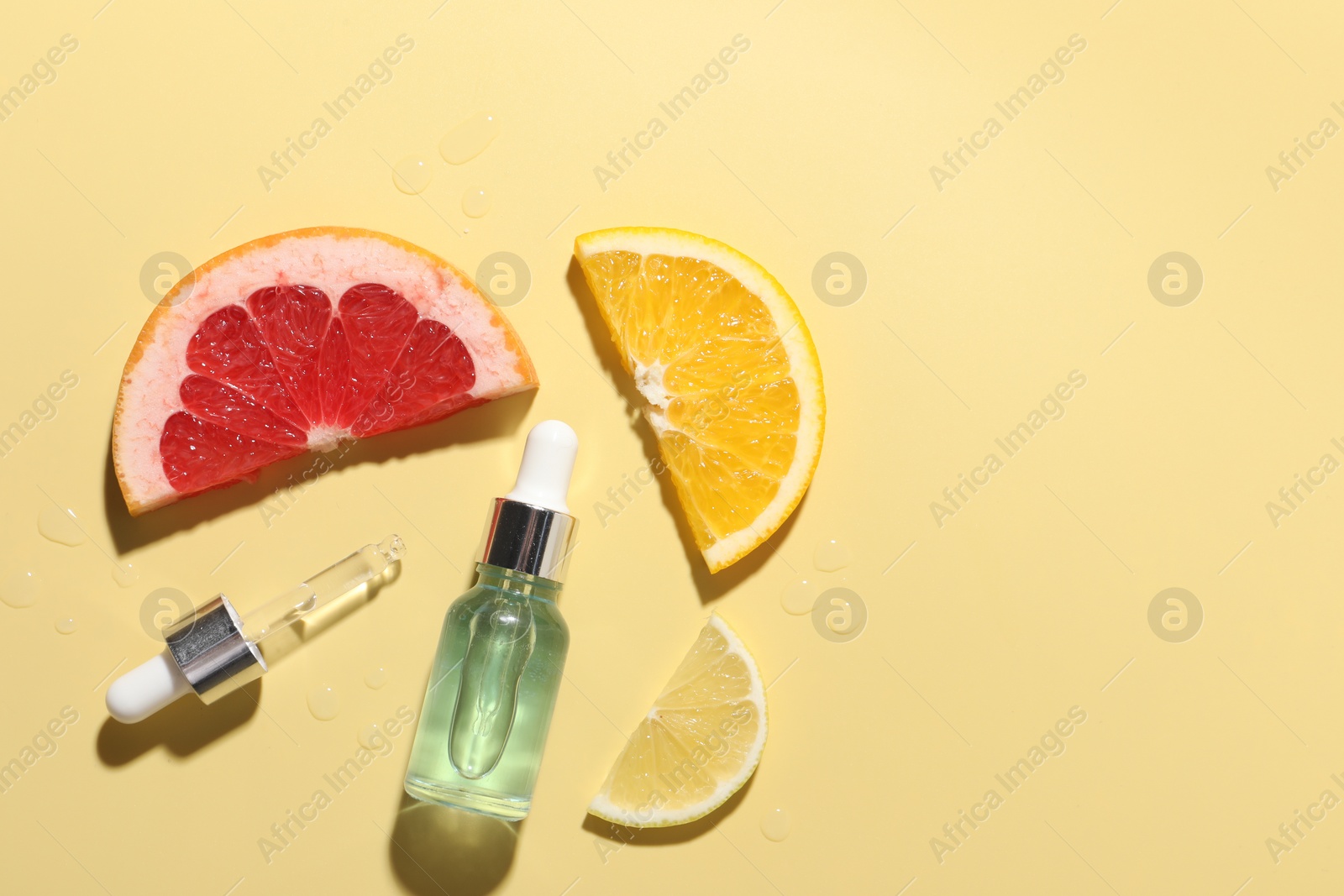 Photo of Bottle of cosmetic serum and sliced citrus fruits on yellow background, flat lay. Space for text