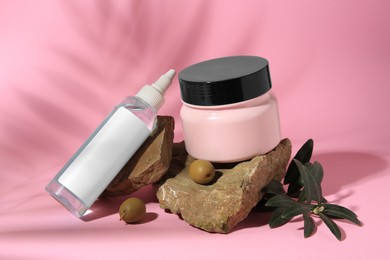 Cosmetic products and olives on pink background
