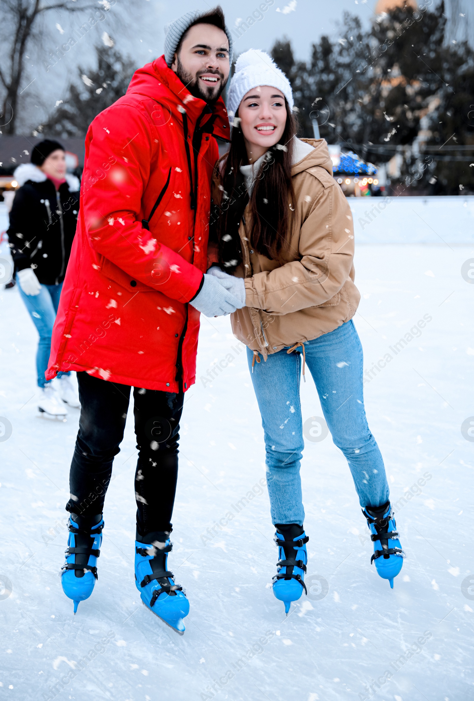 Image of Happy young couple skating at outdoor ice rink