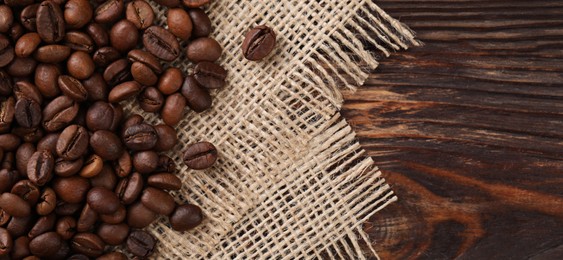 Many coffee beans and burlap fabric on wooden table, top view. Space for text