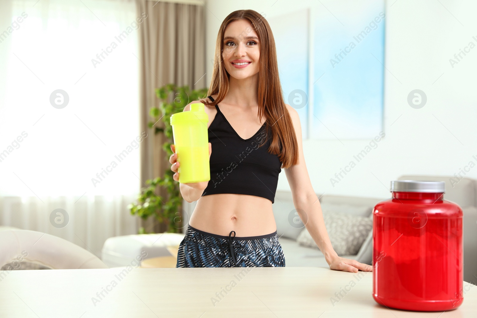 Photo of Young woman with bottle of protein shake at home