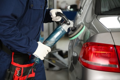 Photo of Technician polishing car body with tool at automobile repair shop, closeup