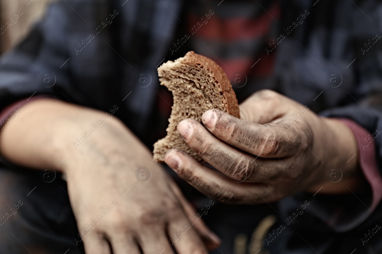 Photo of Poor homeless child with piece of bread outdoors, closeup