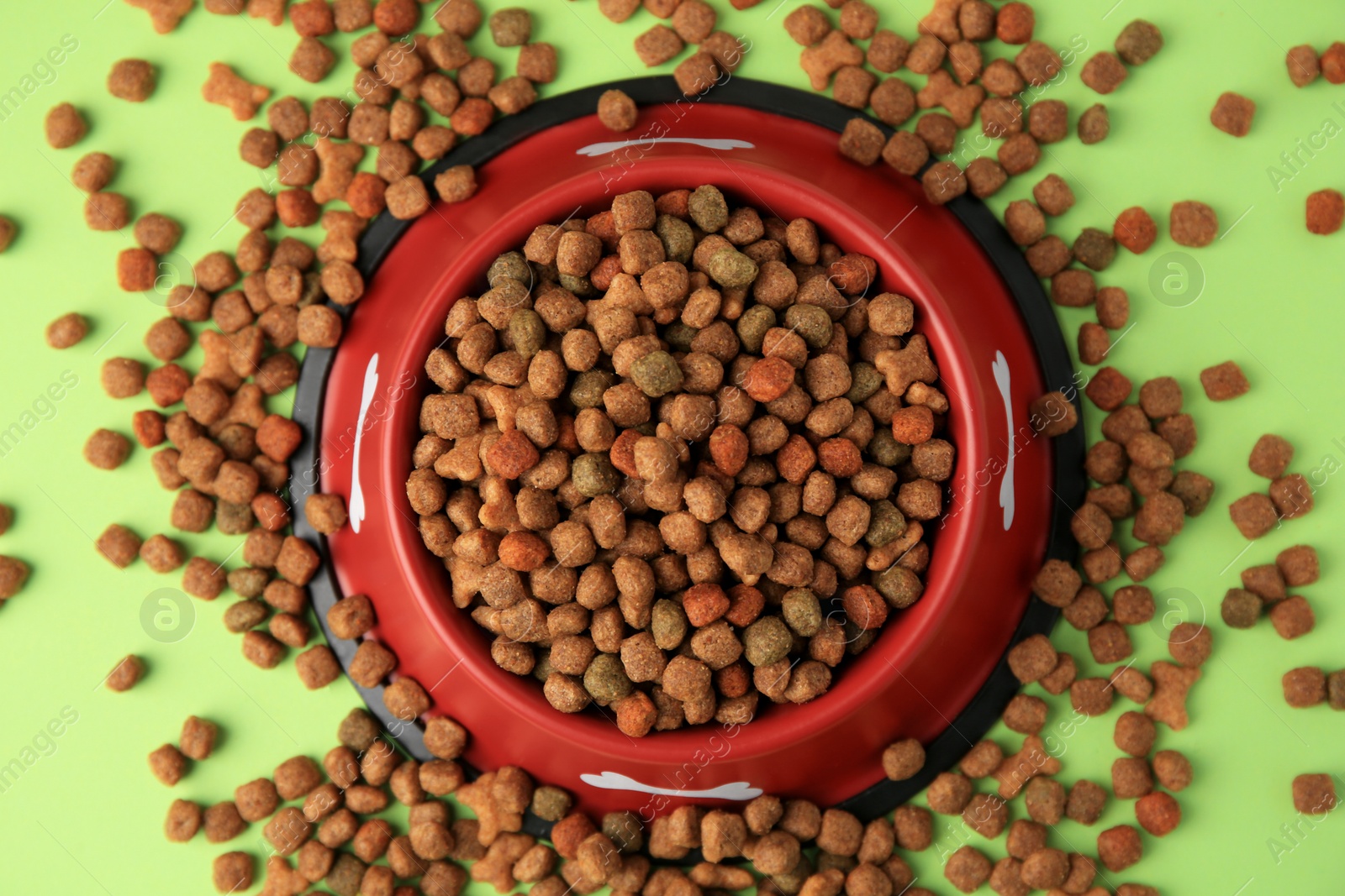 Photo of Dry dog food and feeding bowl on light green background, flat lay