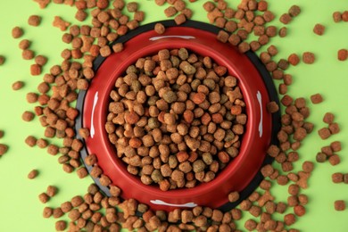 Dry dog food and feeding bowl on light green background, flat lay