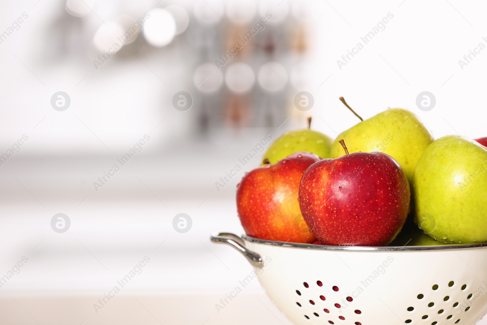 Photo of Colander with different sweet apples on table in kitchen, closeup. Space for text