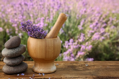 Photo of Spa stones, fresh lavender flowers and mortar on wooden table outdoors, closeup. Space for text