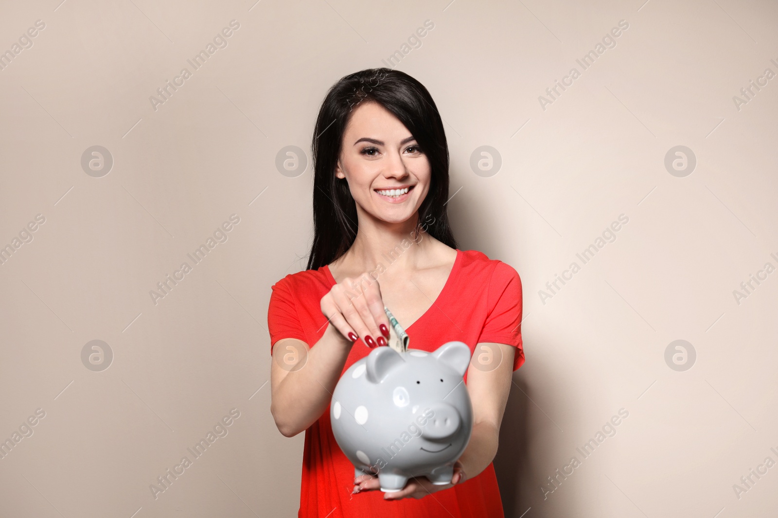 Photo of Beautiful woman putting money into piggy bank on color background