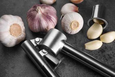 Photo of Garlic press, bulbs and cloves on grey table, closeup