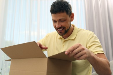 Photo of Happy man opening parcel indoors. Internet shopping