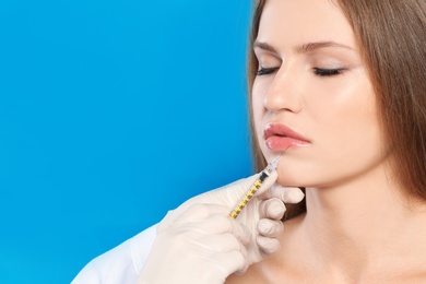 Photo of Young woman getting lips injection on color background, space for text. Cosmetic surgery