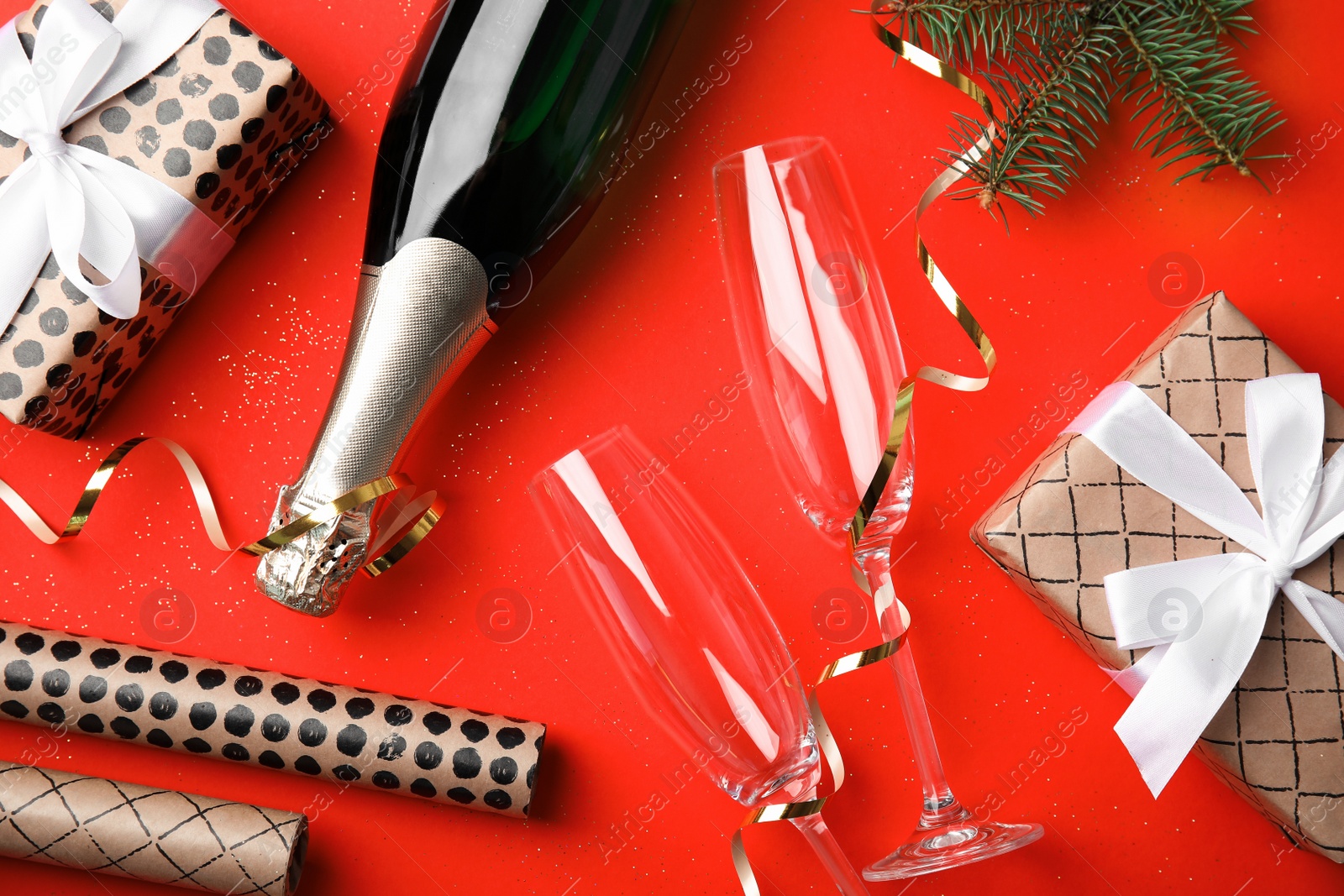 Photo of Christmas composition with bottle of champagne and glasses on red background, top view